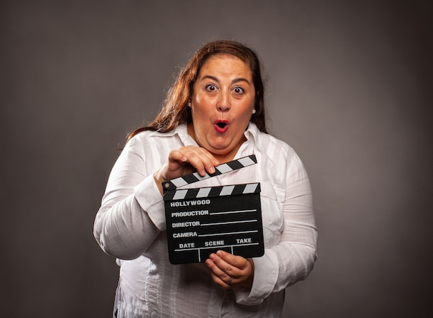 Overweight woman holding a movie clapper board on a grey background