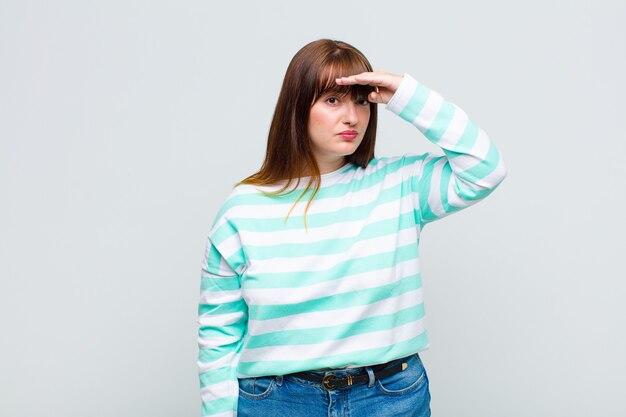 Overweight woman looking bewildered and astonished, with hand over forehead looking far away, watching or searching