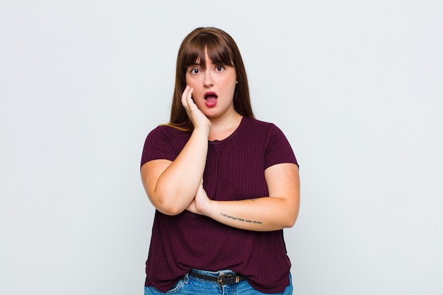 Overweight woman open-mouthed in shock and disbelief, with hand on cheek and arm crossed, feeling stupefied and amazed