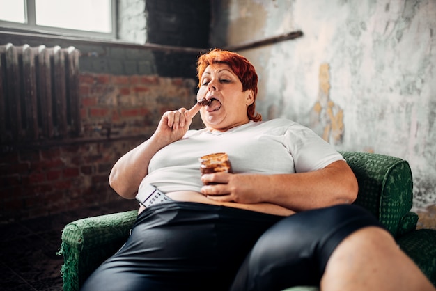 Overweight woman sits in a chair and eats sweets