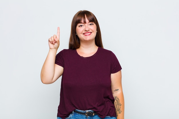 Overweight woman smiling cheerfully and happily, pointing upwards with one hand to copy space