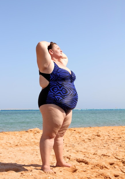 Photo overweight woman standing on beach with hands up