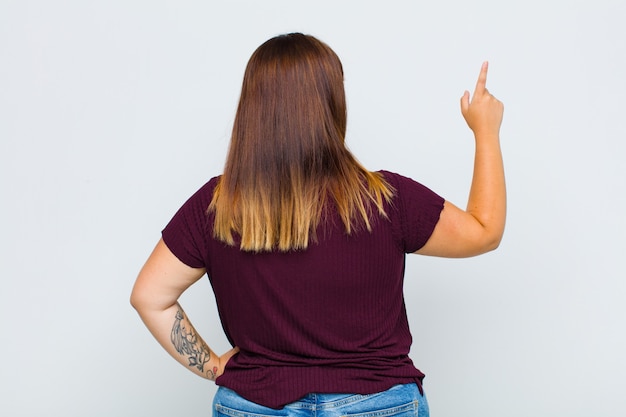 Foto donna in sovrappeso in piedi e che punta a un oggetto sullo spazio della copia, vista posteriore