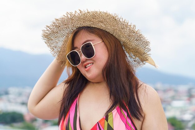 Overweight young asian woman wearing orange swimsuit and straw beach sun hat relaxing in pool Happy plus size woman cheery funny Vacation Traveling in summer