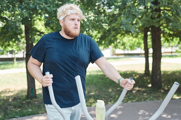 Overweight young man exercising on sports equipment in the park