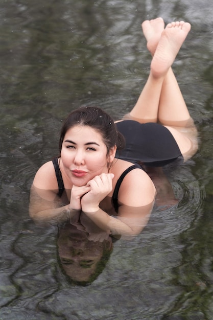 Overweight young woman in black onepiece bathing suit lying in outdoors pool at balneotherapy spa