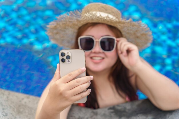 Overweight young woman orange swimsuit relaxing and holding smartphone in swimming pool obese woman vacation traveling hand using phone