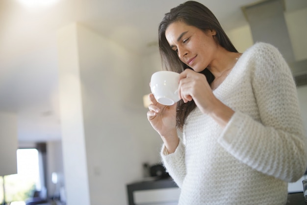 Overweldigende donkerbruine vrouw met kop van koffie in moderne keuken