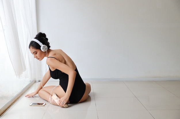 Overweldigende vorm van charmante Aziatische vrouw die zwarte sportkledingszitting met hoofdtelefoon draagt. Mooie vrouw het luisteren muziek van mobiele telefoon terwijl het ballet dansen