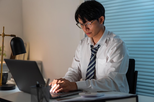 Overwerkconcept De man die aan zijn bureau zit en zich concentreert op het werken via zijn computerlaptop