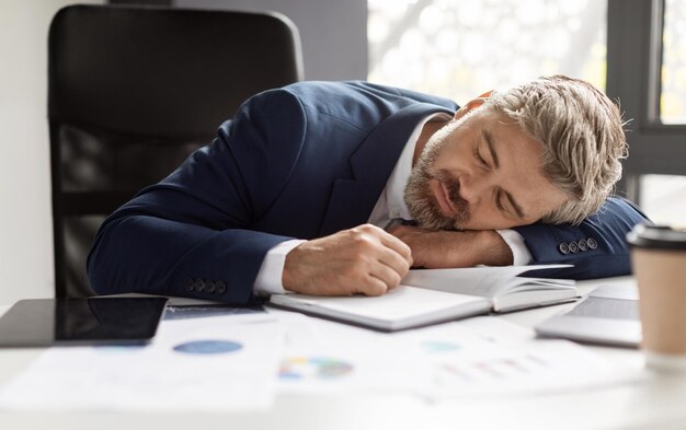 Overwerkconcept uitgeput volwassen zakenman slapen op werkplek in modern kantoor