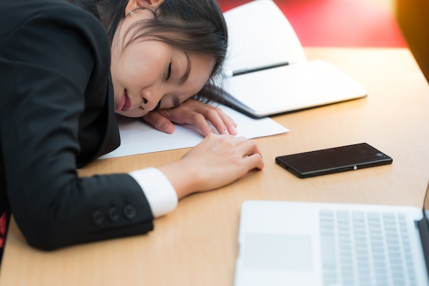 Overwerkt en moe zakenvrouw slapen over een bureau op het werk in haar kantoor.