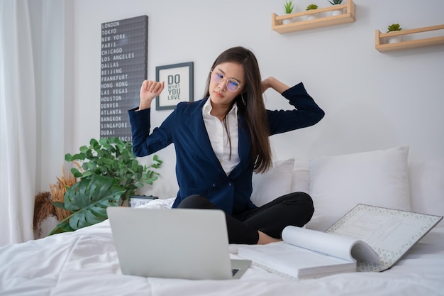 Overwerkte en gestresseerde jonge Aziatische vrouw die aan een laptop werkt en documenten schrijft