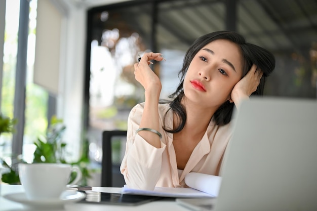 Overwerkte en vermoeide millennial Aziatische zakenvrouw zit aan haar bureau gebrek aan energie