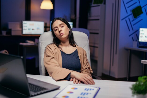 Overwerkte gestresste vrouw die in de loop van de deadline de rugleuning van de stoel leunt. Werknemer valt in slaap terwijl hij 's avonds laat alleen op kantoor werkt voor een belangrijk bedrijfsproject.