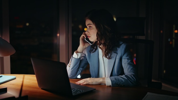 Overwerkte zakenvrouw die's nachts laat aan de telefoon praat op kantoor laptop close-up
