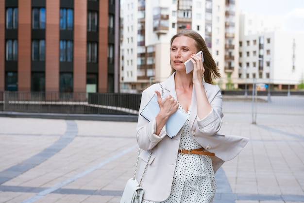 Overwerkte zakenvrouw multitasking zakenvrouw praten op een mobiele telefoon in een lichte jas ne...