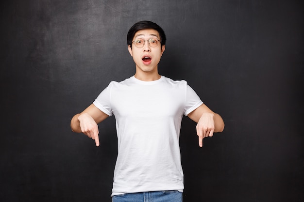 Overwhelmed and excited asian guy in glasses losing his mind over thrilling cool new game, pointing fingers down showing friends what he got with special discount, 