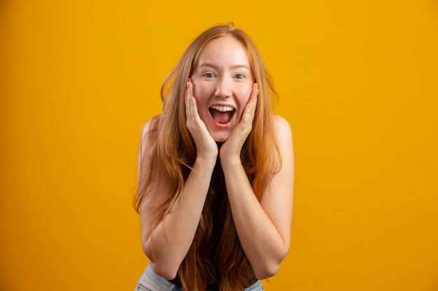 Overwhelmed excited smiling, happy redhead girl celebrating amazing news, achieve victory, winning competition, triumphing as become champion, gain goal or unexpected lucky event happened. On yellow.