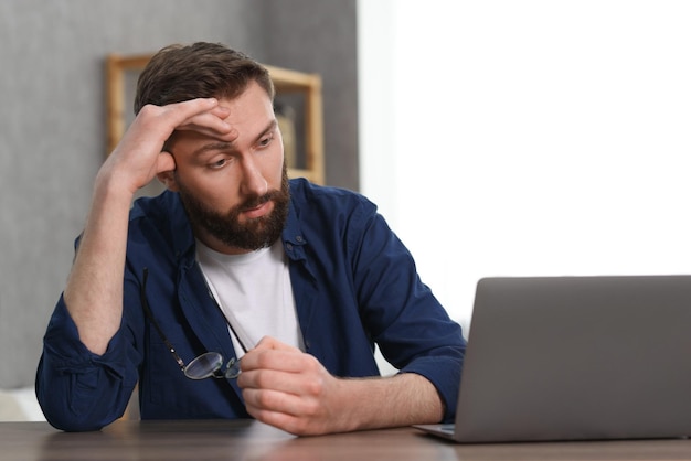 Overwhelmed man sitting with laptop at table indoors