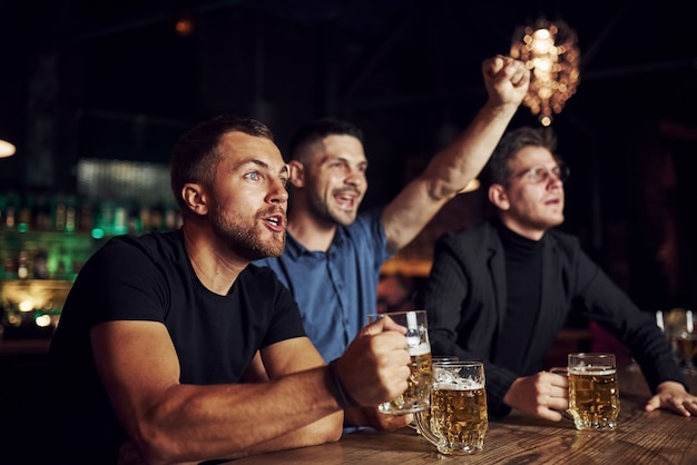 Overwinning vieren. Drie sportfans in een bar voetbal kijken. Met bier in handen.