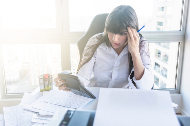 Foto overwogen jonge onderneemster die calculator op het werk bekijkt