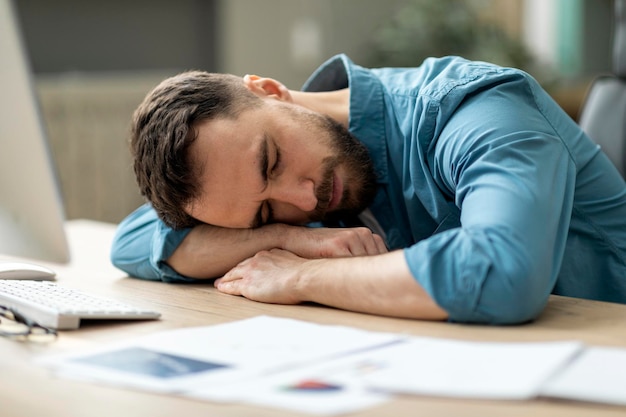 Overwork concept exhausted male employee sleeping at desk with papers in office