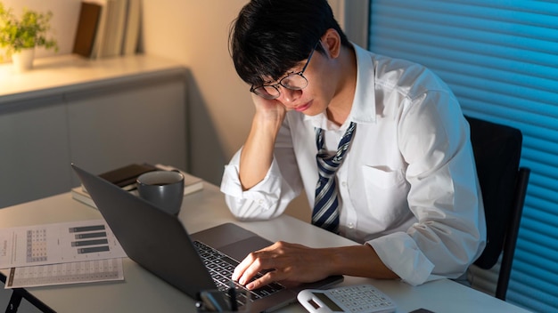 과로 개념 책상에 앉아 컴퓨터 랩톱을 통해 작업하는 데 집중하는 남자