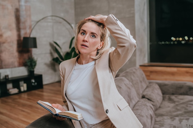 Overworked blonde American businesswoman in suit holds diary touches head tired thinks of deadline