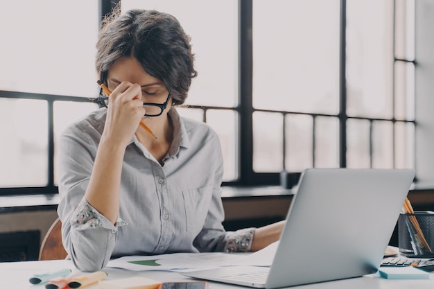 Overworked business lady suffering from headache while working remotely from home