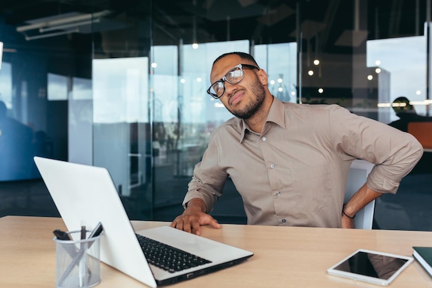 Overworked businessman back pain african american man massaging\
back man working sitting on chair