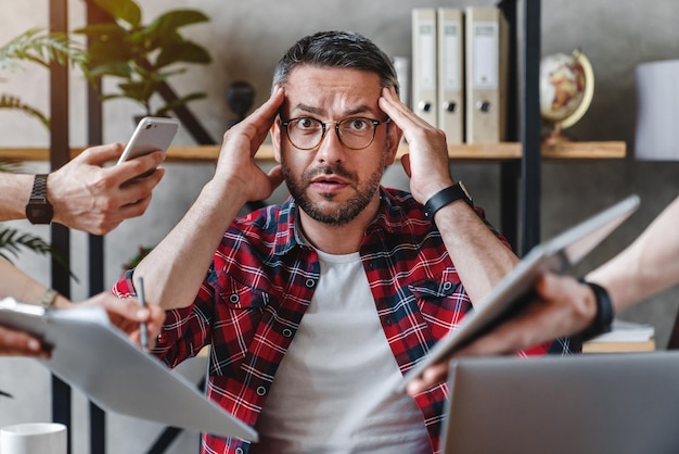 Uomo d'affari oberato di lavoro seduto al computer portatile sovraccarico di lavoro più compiti in un ufficio moderno