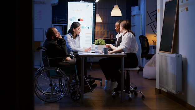 Фото Перегруженный работой бизнесмен-инвалид в инвалидной коляске игнорируется во время работы в конференц-зале бизнес-офиса компании поздно ночью