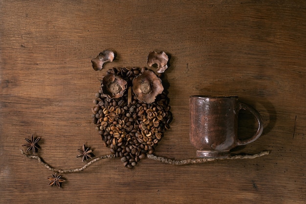 Forma di gufo da chicchi di caffè e spezie. il gufo si siede sul ramo con la tazza di caffè sopra fondo di legno. concetto di caffè misterioso divertente