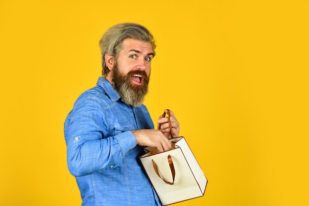 Own business bearded man hold paper bag presents Delighted man shopping online hipster open purchase at electronics store Positive man enjoying shopping copy space