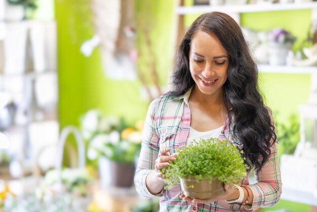 The owner of the flower shop is holding a flower pot with herbs