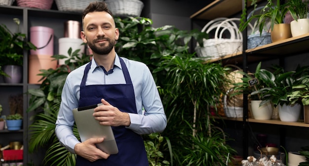 The owner of the garden center with a tablet in his hands next to the shelves perfect plants