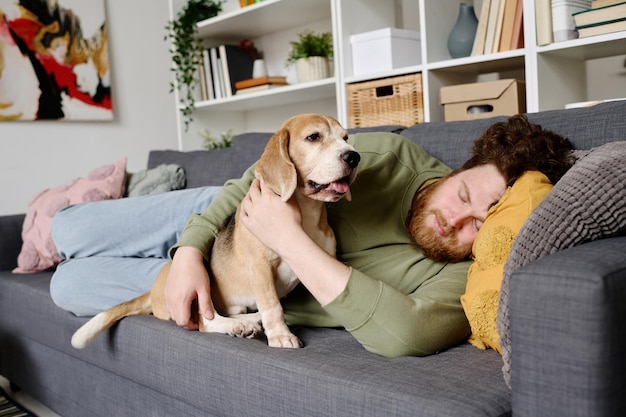 彼の犬と一緒にソファで寝ている所有者