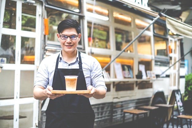 The owner of a small coffee shop welcomes customers in front of the coffee shop with a smile and a cup of coffee in hand. SME Business owner concept.