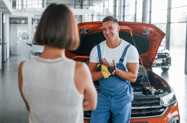 屋内で自動車を修理している男性の近くに立っている所有者 専門的なサービス