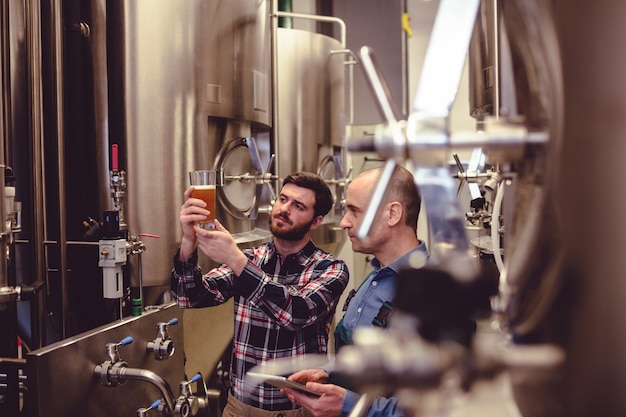 Foto proprietario ed operaio che esaminano birra in vetro