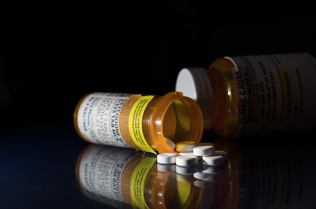 オキシコドンは、一連のオピオイド鎮痛錠の総称です。オキシコドン錠の処方ボトルと反射のあるガラステーブル上の丸薬
