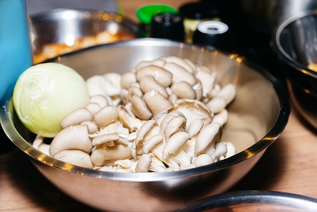 Oyster mushrooms in a metal bowl on a wooden table with peeled onion Raw ingredients before cooking