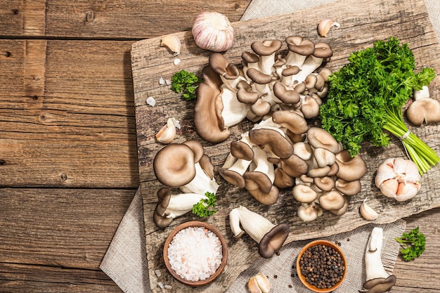 Oyster mushrooms ready for cooking Fresh parsley spices and garlic Trendy hard light dark shadows old wooden background top view