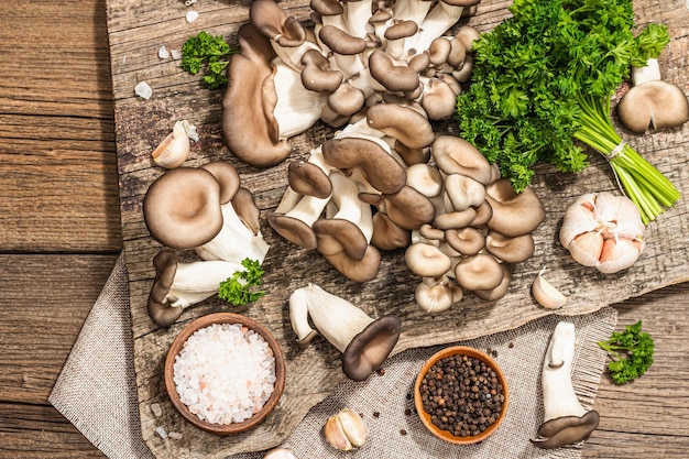 Oyster mushrooms ready for cooking Fresh parsley spices and garlic Trendy hard light dark shadows old wooden background top view