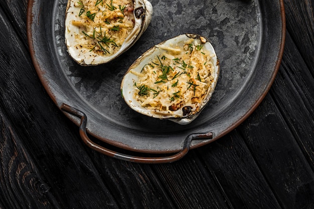 Oysters baked with cheese and herbs served on a rustic metallic plate shot on wooden backgrond top view