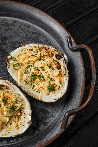 Oysters baked with cheese and herbs served on a rustic metallic plate shot on wooden backgrond top view