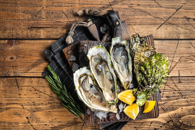 Oysters served on wooden board with ice and lemon. Wooden background. Top view.