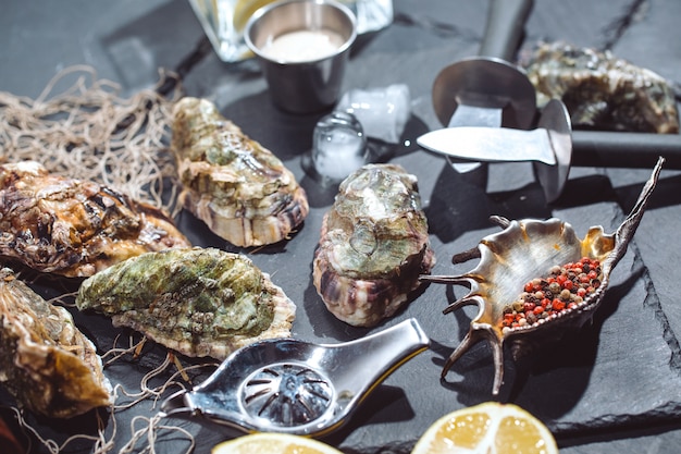 Oysters on stone plate with ice, lemon, fishing net, pepper and knife. 