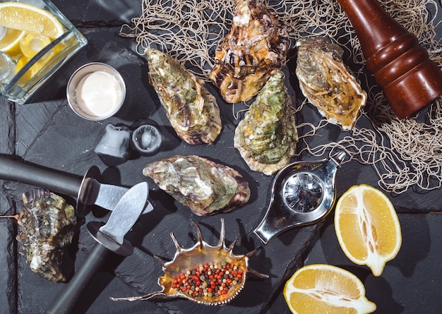 Photo oysters on stone plate with ice, lemon, fishing net, pepper and knife.